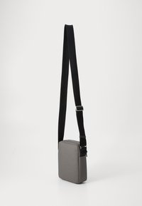 Borsa a spalla grigia con forma rettangolare, materiale in tessuto, tracolla nera regolabile e dettagli in cerniera argentata. Design semplice ed elegante.