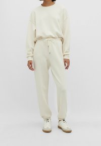 Crèmekleurige, relaxte sweatshirt en bijpassende joggers van zachte stof, met een ronde halslijn en elastische boorden, gecombineerd met sneakers.