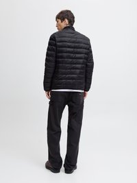 Black puffer jacket with horizontal quilted texture, high collar, and minimal detailing, worn with black cargo pants and shoes.