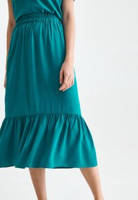 Jupe teal, jusqu'aux genoux, avec une taille élastique et un ourlet volé. Fabriquée en tissu lisse, mettant en valeur une silhouette fluide.