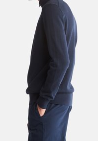 Suéter azul marino con cuello alto, puños y dobladillo de canalé; fabricado en suave tejido de punto; incluye un pequeño y sutil logo en el pecho.