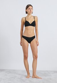 Fekete fehérnemű szett, mely háromszög alakú, vékony pántos melltartóból és hozzá illő, alacsony derekú, csipke díszítésű tanga bugyiból áll. Egységes, sima textúrájú anyagból.