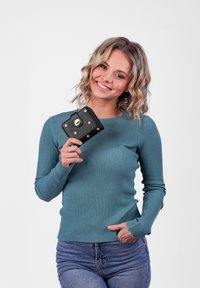 Teal ribbed sweater with long sleeves, paired with a small black wallet featuring gold accents and pink studs, held against a plain background.