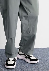Pantaloni larghi grigi con una texture liscia e tasche laterali, abbinati a sneakers bianche e nere con un design stratificato e lacci.