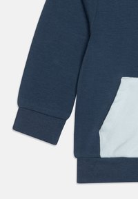 Felpa blu navy con tessuto testurizzato, dotata di una tasca azzurra e polsini a coste. Design semplice senza motivi.