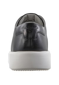Černé kožené tenisky s hladkým povrchem, bílé gumové podrážky a embosované logo "Strellson" na zadní straně. Minimalistický design.