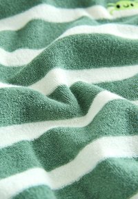 Zöld és fehér csíkos törölköző, texturált pamut anyagból, puha, plüss tapintással. Jellegzetes kis zöld díszítés egyszerű mintával.
