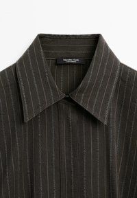 Dark striped collared shirt featuring a label that reads "Massimo Dutti," emphasizing classic design and craftsmanship.