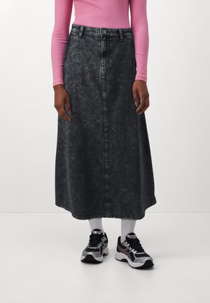 Osoba nosząca czarną midi spódnicę jeansową acid wash, różowy top z długim rękawem, białe skarpetki i czarno-białe buty sportowe, stojąca.