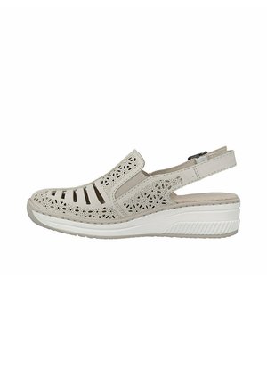 Dichte beige sandaal met bloemmotief uitsparingen, elastisch zijpaneel, verstelbare hielband en gewatteerde witte sleehakzool.