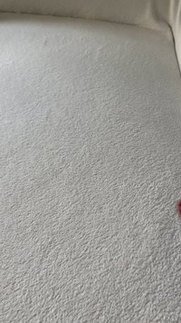 Tessuto grigio chiaro con una texture morbida, caratterizzato da un motivo sottile. L'angolo presenta un piccolo accento di rosso scuro.