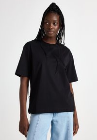 Black oversized t-shirt made of cotton, featuring a crew neckline and short sleeves, paired with light blue denim jeans.