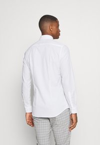 Witte lange mouwen shirt met een traditionele kraag, gestructureerde stof en manchetten met één knoop, gecombineerd met grijs geblokte broek.