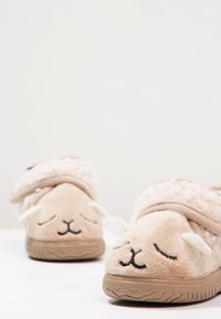 Chaussons en fleece beige en forme de mouton, avec des détails faciaux brodés, des accents duveteux et une semelle texturée pour une meilleure adhérence.
