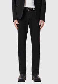 Svarta byxor i slät tyg, med en slim fit design. Tillsammans med ett flätat läderbälte och svarta skor.