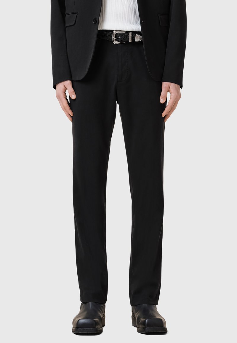 Svarta byxor i slät tyg, med en slim fit design. Tillsammans med ett flätat läderbälte och svarta skor.