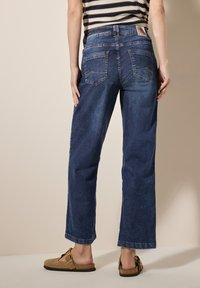 Donkerblauwe denim wijde jeans met twee achterzakken en een riemlus. Gecombineerd met lichtbruine instappers.