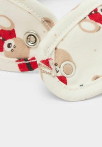 Tessuto di cotone color crema con motivo di orsetti in marrone, rosso e verde; presenta bottoni a pressione in metallo e bordi cuciti.