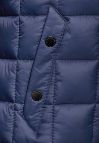 Navy puffer jacket featuring quilted texture, black buttons, and a flap pocket design. The material appears shiny and lightweight.