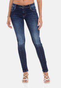 Donkerblauwe skinny jeans met een vervaagd ontwerp, vijf-pocketstijl en een knoopsluiting. Voorgesteld met lichtbruine stiksels.