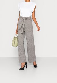 Pantaloni ampi in misto lino grigio con vita alta e cintura, abbinati a una maglietta bianca a maniche corte e tacchi a punta neri. Inclusa una borsa verde chiaro.