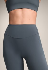 Hochgeschnittene Sportleggings in einem gedeckten Grauton, mit einer glatten Textur und minimalem Nahtdetail für ein schlankes Erscheinungsbild.