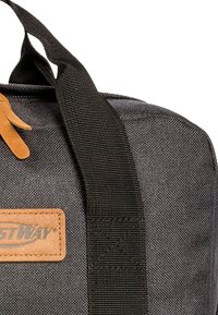 Zwarte stoffen duffelbag met duurzame handvatten, een tan leren logo patch en een gestructureerd oppervlak. Aangekleed met zwarte webbing.