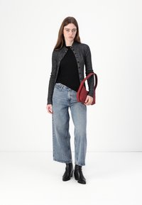 Svart langermet knapp cardigan over en svart topp, paret med vide lysvaskede jeans og ankelstøvler. Bærer en burgunder skulderveske.