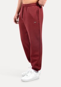 Vinröda mjukisbyxor med elastisk midjeresår, sidfickor och avsmalnande mudd. Bärs med vita sneakers för kontrast.