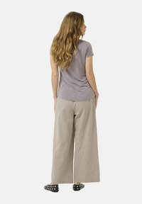 T-shirt gris à manches courtes, associé à un pantalon large beige clair à rayures, et des chaussures noires à enfiler décorées de clous en argent.