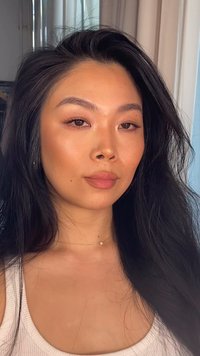 Porträtt av en person med långt svart hår, en ljusbeige topp och ett fint guldhalsband med en liten pärla. Huden har en naturlig lyster.