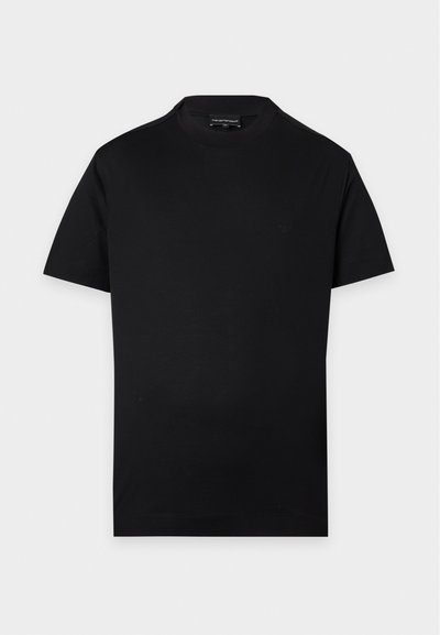 Απλό μαύρο κοντομάνικο T-shirt με στρογγυλή λαιμόκοψη, διακριτικό μικρό λογότυπο στο στήθος και ορατή ετικέτα στον λαιμό σε γκρι φόντο.