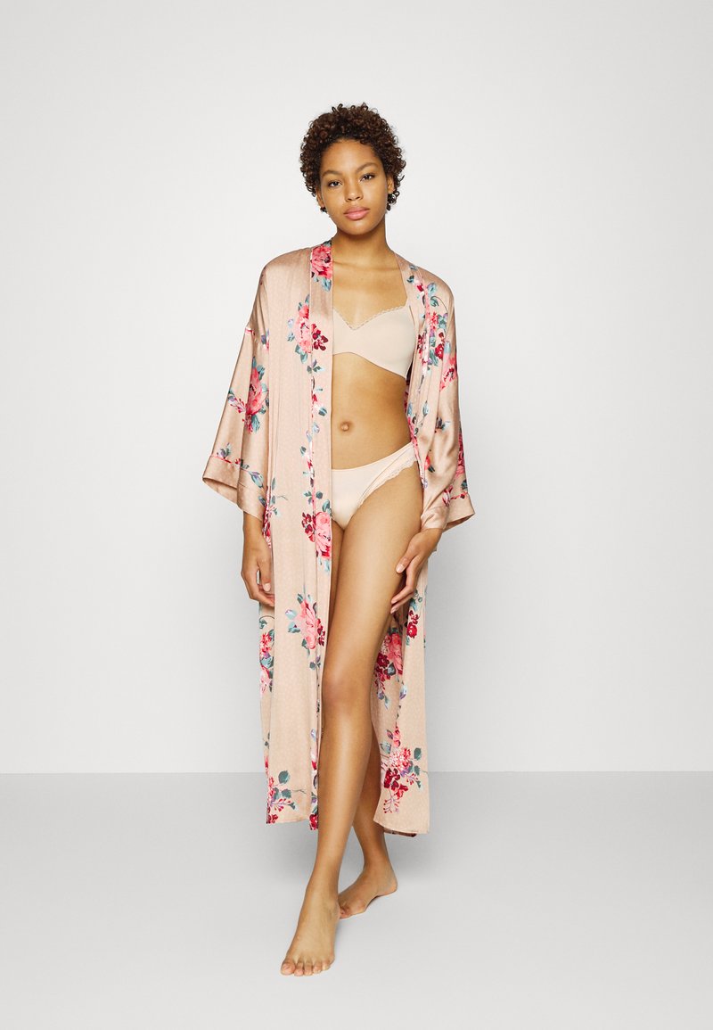 Lange, bloemenpatronen kimono van zachte, lichte stof, in blushroze kleur, met brede mouwen en een open voorkant, gedragen over beige lingerie.