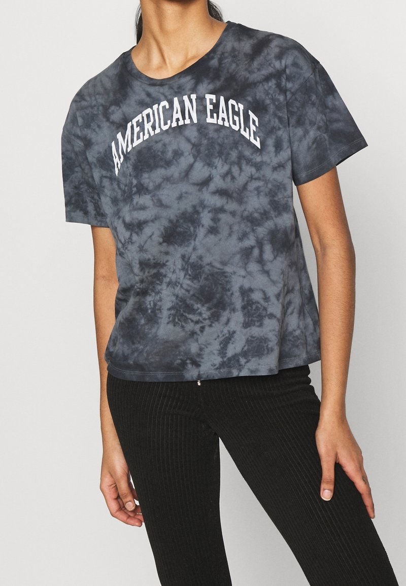 T-shirt à manches courtes, tie-dye gris foncé avec le texte "AMERICAN EAGLE" en blanc sur la poitrine. Tissu doux avec une coupe décontractée.