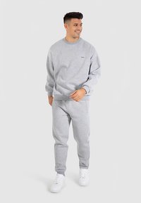 Gray sweatshirt with round neck and logo, paired with matching gray sweatpants. Worn with white sneakers, featuring a relaxed fit.