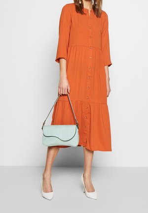 Ruskiloinen napillinen mekko, jossa on kerroksellinen helma, yhdistettynä teksturoituun mintunvihreään käsilaukkuun ja valkoisiin teräväkärkisiin korkokenkiin.