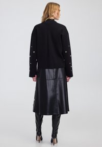 Maglione nero con vestibilità oversize, caratterizzato da dettagli metallici sulle maniche. Abbinato a una gonna midi in pelle nera e stivali neri alti.