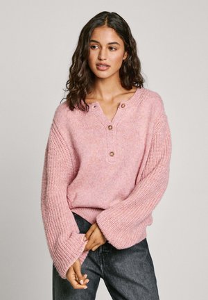 Rosa gestrickter Pullover mit lockerer Passform, der über einen Knopfverschluss am Ausschnitt und weite Ärmel verfügt. Strukturiertes Gewebe und subtile Farbvariationen im gesamten Pullover.