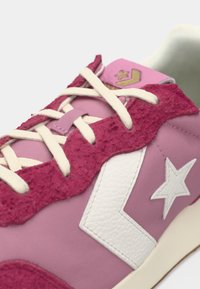 Pink sneaker with textured magenta accents, white star logo, and cream laces. Features a mix of smooth and fuzzy materials.