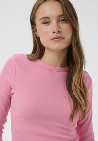 Rózsaszín bordázott hosszú ujjú felső kerek nyakkivágással és testhez simuló szabással. Simább textúrájú, minimális díszítéssel.