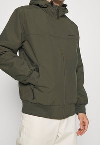 Olivgrüne Kapuzenjacke mit Vorderreißverschluss, elastischen Bündchen und Seitentaschen. Glatte Textur mit minimalistischer Gestaltung und Logo-Detail.