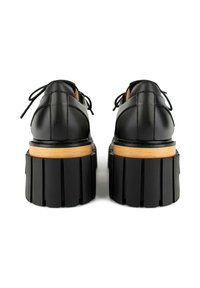 Pantofi din piele neagră, cu vârfuri rotunde, având talpă platformă texturată neagră și accente din lemn, legați cu șireturi subțiri negre.