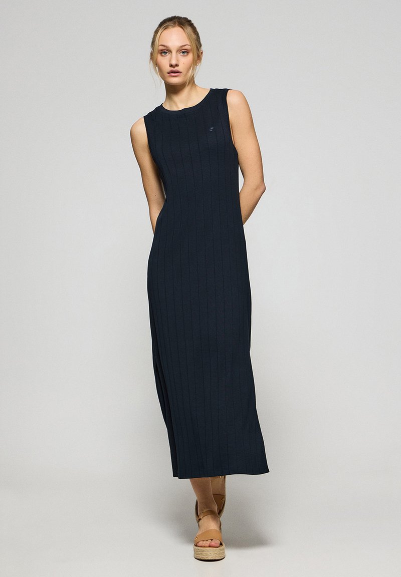 Sukienka bez rękawów w kolorze granatowym z pionowym żebrowanym wzorem, długość do kostek i bocznymi rozcięciami. Zestawiona z beżowymi espadrylami.