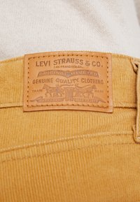 Parche de cuero de Levi Strauss & Co. en tela de pana amarilla, con texto en relieve, diseño de remaches y elementos gráficos detallados.