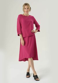 Completo a due pezzi fucsia con top a maniche corte e gonna al ginocchio, caratterizzato da una vestibilità comoda, tessuto morbido e mule nere con punta aperta.