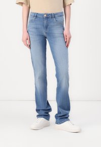 Light blue denim jeans with a straight fit, featuring a buttoned waistband, belt loops, and five pockets. Styled with white sneakers.