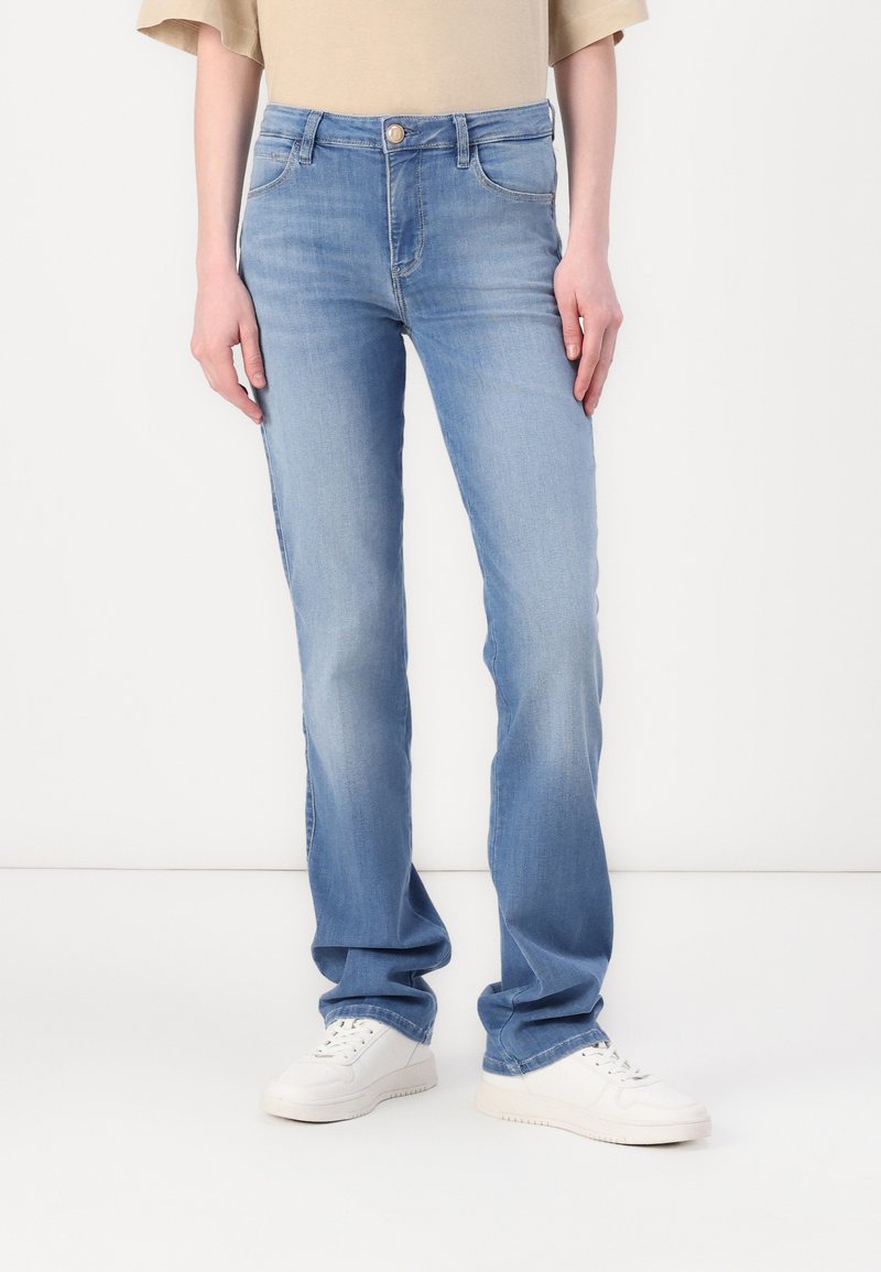 Light blue denim jeans with a straight fit, featuring a buttoned waistband, belt loops, and five pockets. Styled with white sneakers.