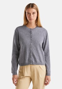 Šedý pletený kardigan s kulatým výstřihem, uzavírání na sedm knoflíků se perlovými detaily a dlouhými rukávy, kombinovaný s béžovými kalhotami.