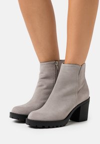 Botines de ante gris con una suela negra gruesa y una cremallera lateral. Punta redondeada y textura suave. Tacón bloque de altura media.