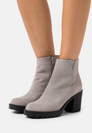 Bottines en suede gris avec une semelle épaisse noire et une fermeture éclair sur le côté. Embout rond et texture lisse. Talon bloc de hauteur moyenne.